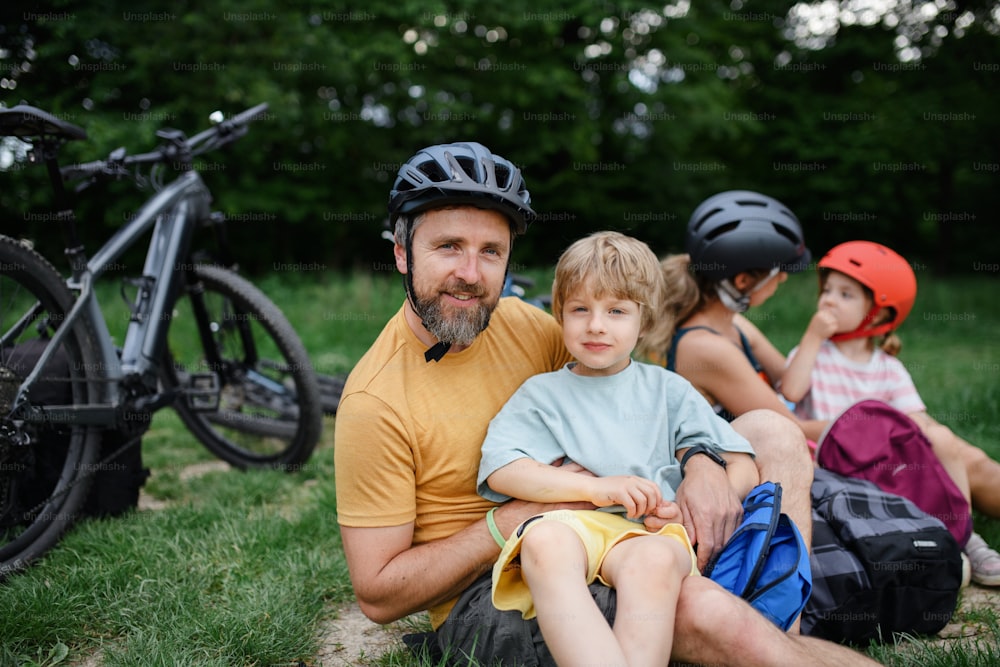 Una giovane famiglia con bambini piccoli che riposano dopo un giro in bicicletta, seduti sull'erba nel parco in estate.