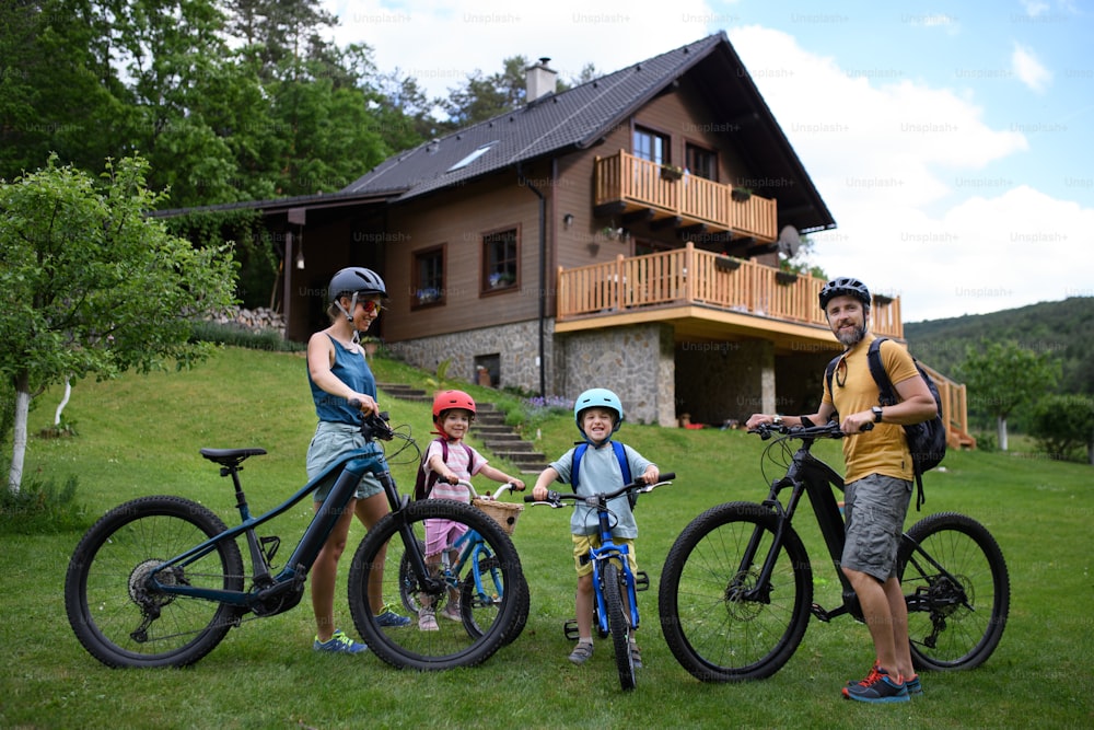 Ein Porträt einer jungen Familie mit kleinen Kindern, die sich auf eine Radtour vorbereiten und mit Fahrrädern vor dem Haus stehen.