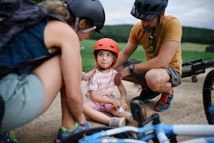 Una madre e un padre che aiutano la loro piccola figlia dopo essere caduti dalla bicicletta all'aperto