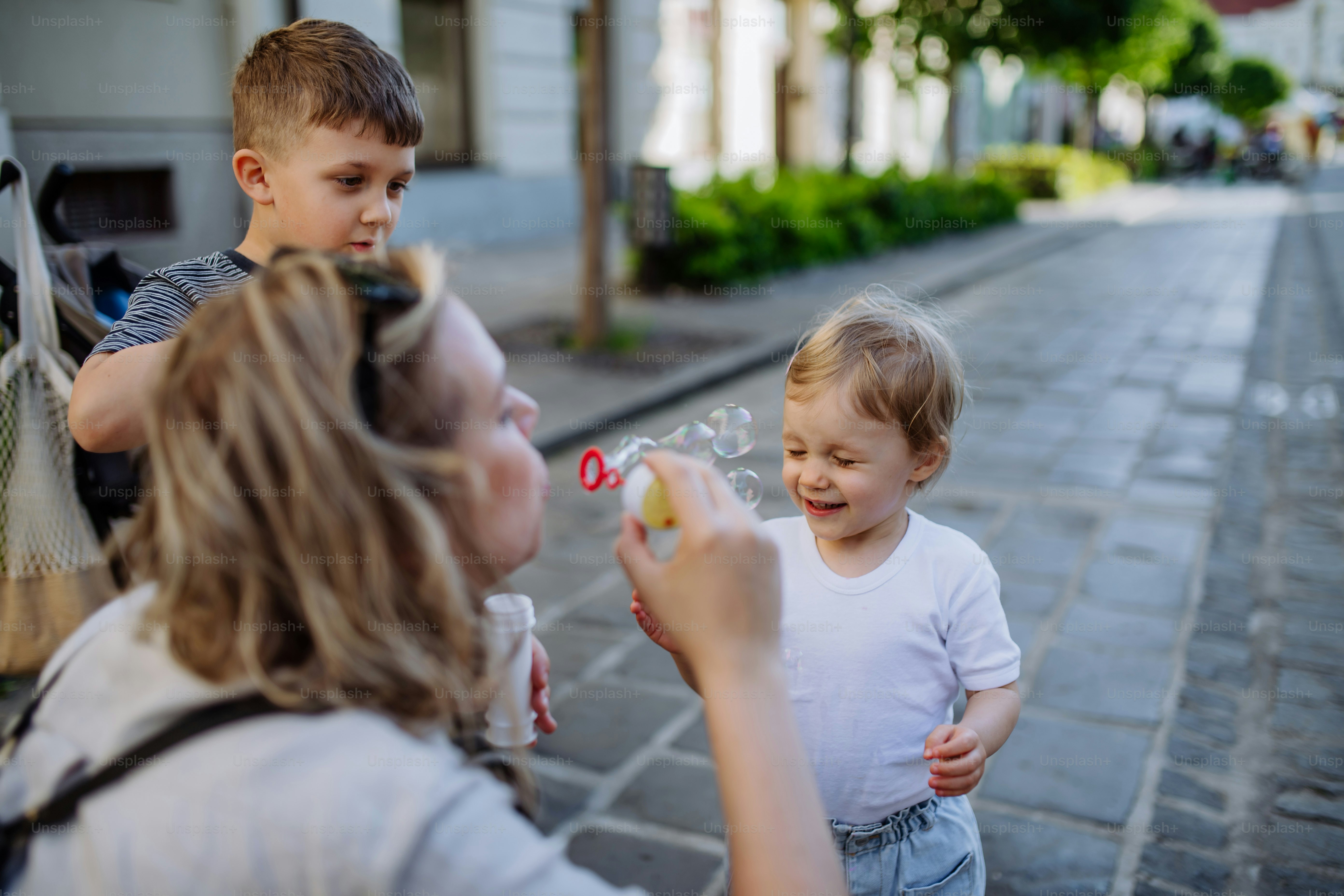 A young mother playing with her kids, blowing bubbles in city street in summer.