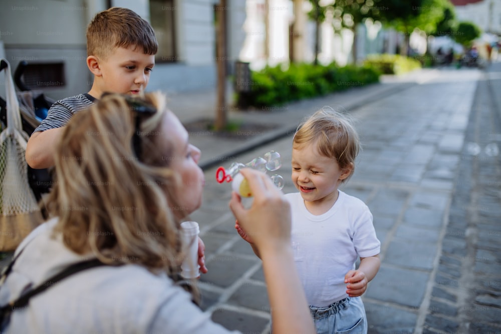 Una giovane madre che gioca con i suoi figli, soffiando bolle nelle strade della città in estate.