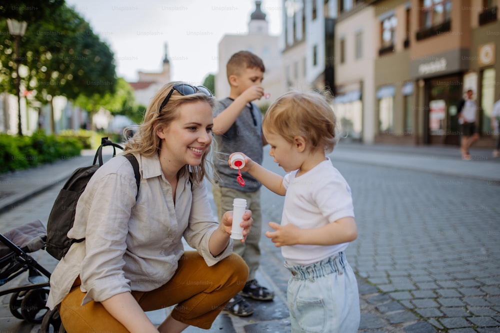 Uma jovem mãe brincando com seus filhos, soprando bolhas na rua da cidade no verão.