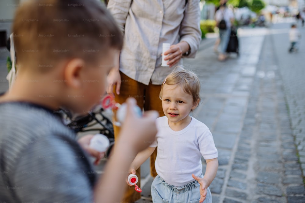 Ein kleiner Junge, der im Sommer mit seiner kleinen Schwester in der Stadtstraße Seifenblasen bläst.