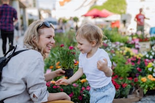 Uma jovem mãe com sua filha pequena comprando flores de vaso no mercado no verão na cidade.