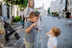 A little boy blowing bubbles with his little sister in city street in summer.
