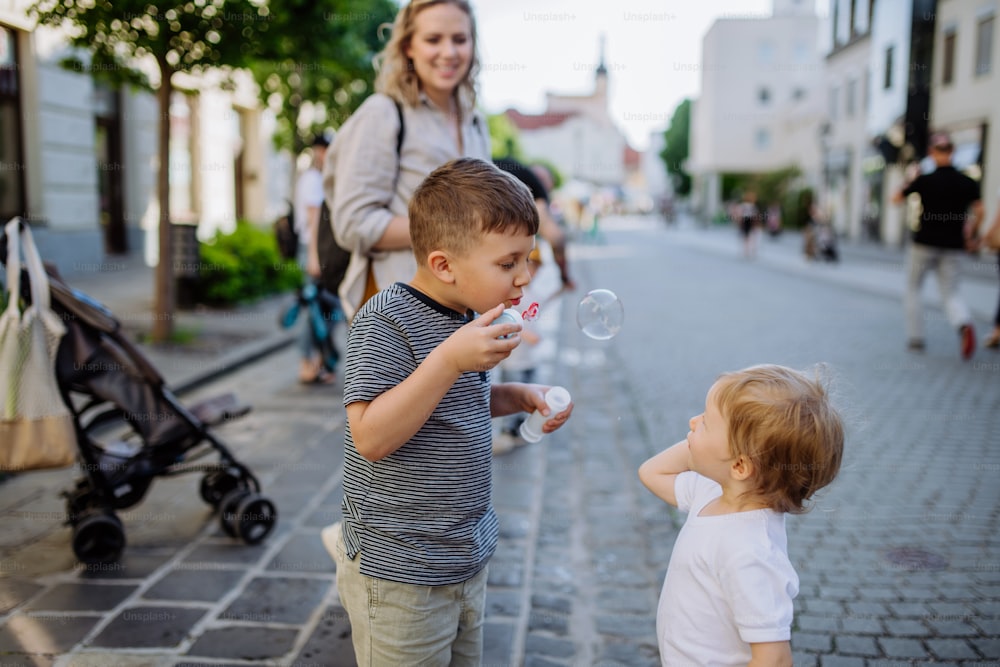 Un petit garçon soufflant des bulles avec sa petite sœur dans la rue de la ville en été.