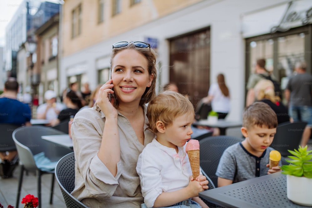 Eine junge Mutter, die im Sommer ein Selfie mit ihren Kindern beim Eisessen im Café im Freien auf der Straße macht.