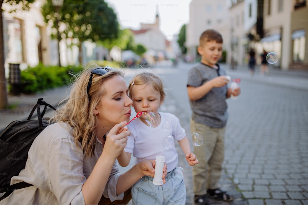 Una giovane madre che gioca con i suoi figli, soffiando bolle nelle strade della città in estate.
