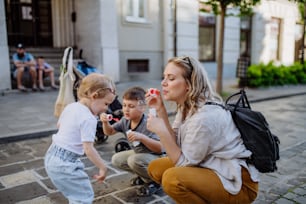 Uma jovem mãe brincando com seus filhos, soprando bolhas na rua da cidade no verão.