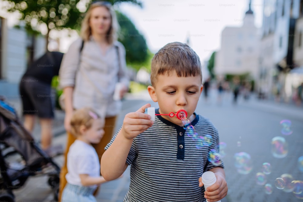 A little boy blowing bubbles in city street in summer.