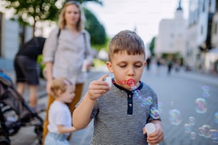 A little boy blowing bubbles in city street in summer.