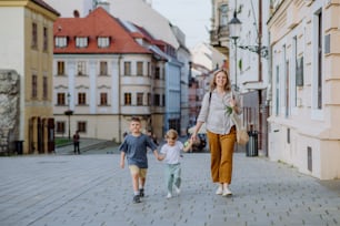 Una giovane mamma con la borsa della spesa zero rifiuti che si tiene per mano con i suoi figli e cammina nel centro storico della città.