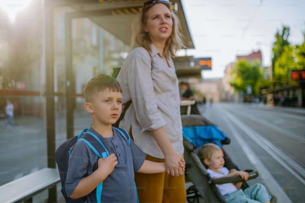 Una giovane madre con bambini piccoli in attesa alla fermata dell'autobus in città.