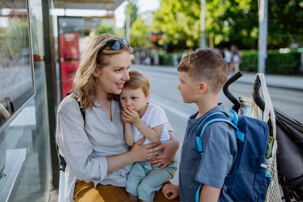 Une jeune mère avec de jeunes enfants attendant à l’arrêt de bus en ville.