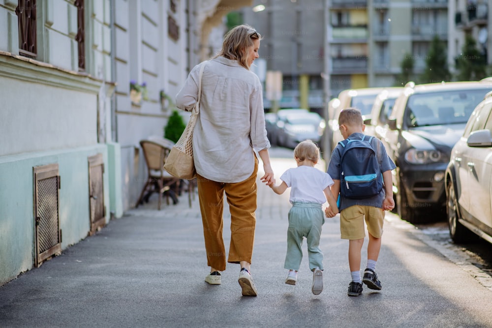 Una joven madre con bolsa de compras cero residuos tomada de la mano con sus hijos y caminando por la calle de la ciudad