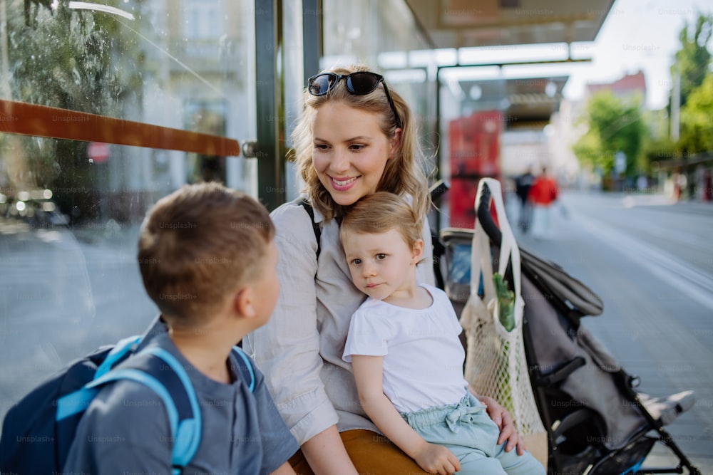 Una joven madre con niños pequeños esperando en la parada de autobús en la ciudad.