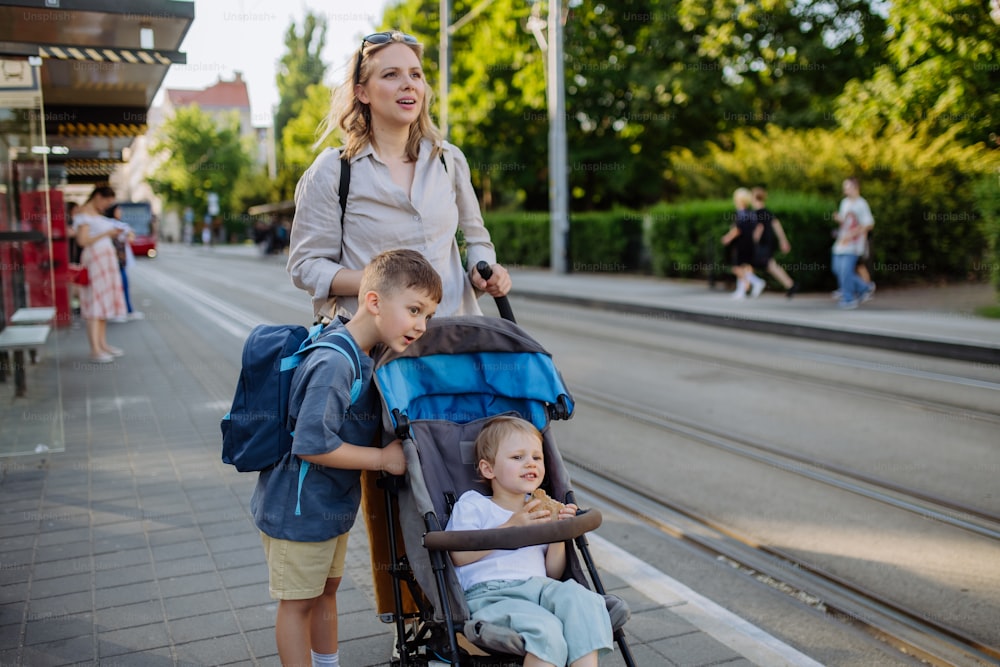 Eine junge Pendlerin mit kleinen Kindern auf dem Weg zur Schule, zu Fuß auf der Straßenbahnhaltestelle in der Stadt.