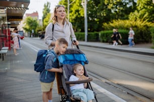Una joven madre que viaja con niños pequeños de camino a la escuela, caminando por la estación de tranvía de la ciudad.