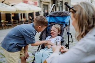 A mother and little brother calming a crying girl sitting in a stroller while walking down the street