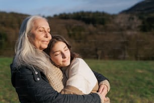 A happy senior grandmother with teenage granddaguhter hugging in nature on spring day.