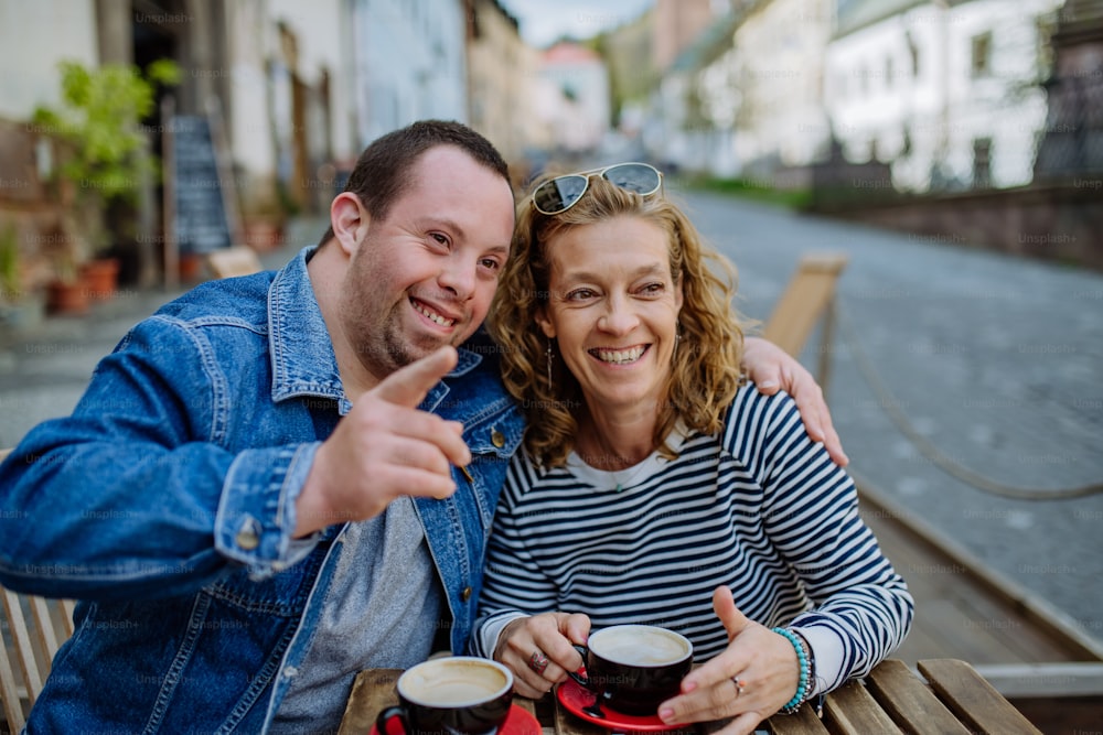 Um retrato de um jovem feliz com síndrome de Down com sua mãe sentada em um café ao ar livre e conversando.