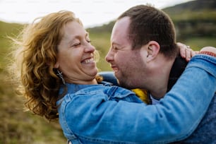 An outdoor portrait of mother hugging her grown up son with Down syndrome, motherhood concept.