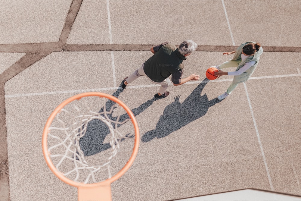 A father and teenage daughter playing basketball outside at court, high angle view above hoop net.A happy father and teen daughter playing basketball outside at court, high fiving.