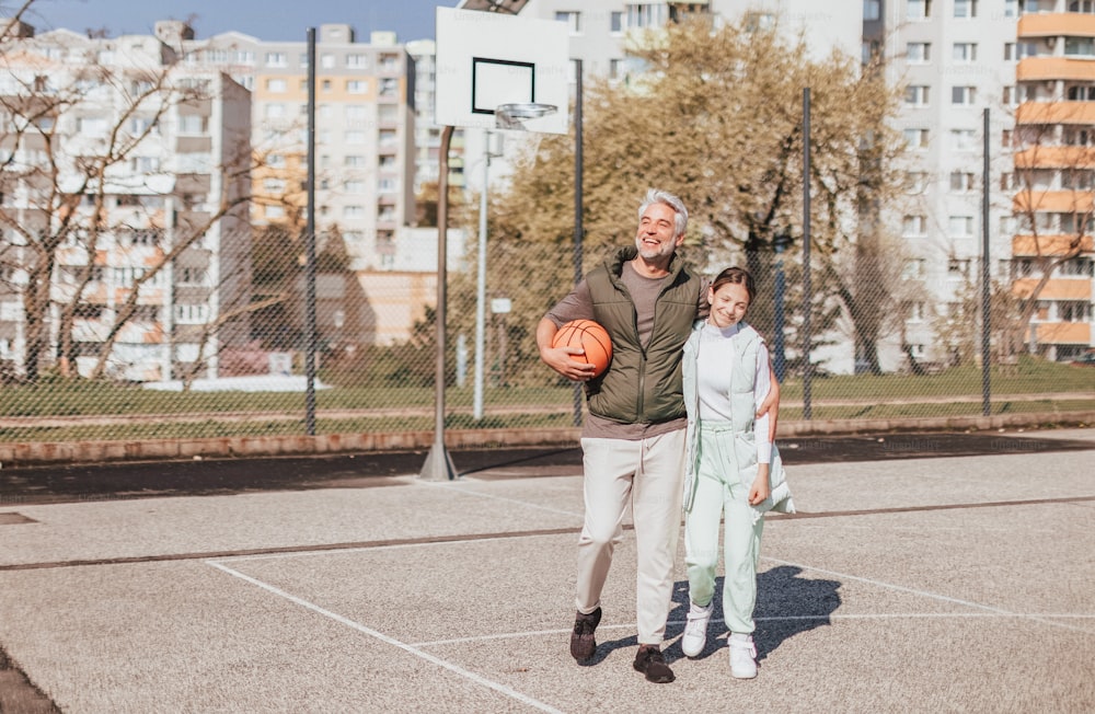 幸せな父と十代の娘が抱き合い、バスケットボールコートで外のカメラを見ている。幸せな父と十代の娘がコートで外でバスケットボールをし、ハイファイブ。