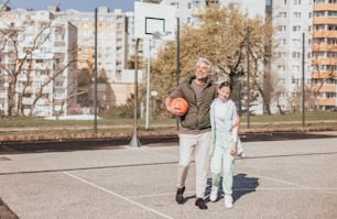A happy father and teen daughter embracing and looking at camera outside at basketball court.A happy father and teen daughter playing basketball outside at court, high fiving.