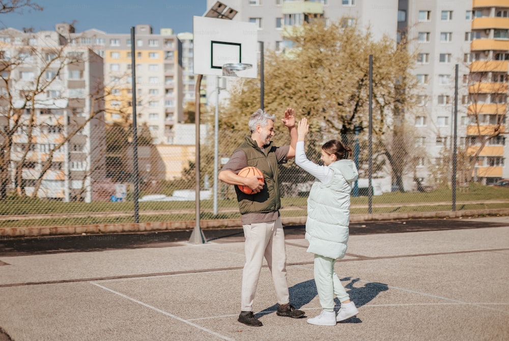 A happy father and teen daughter playing basketball outside at court, high fiving.