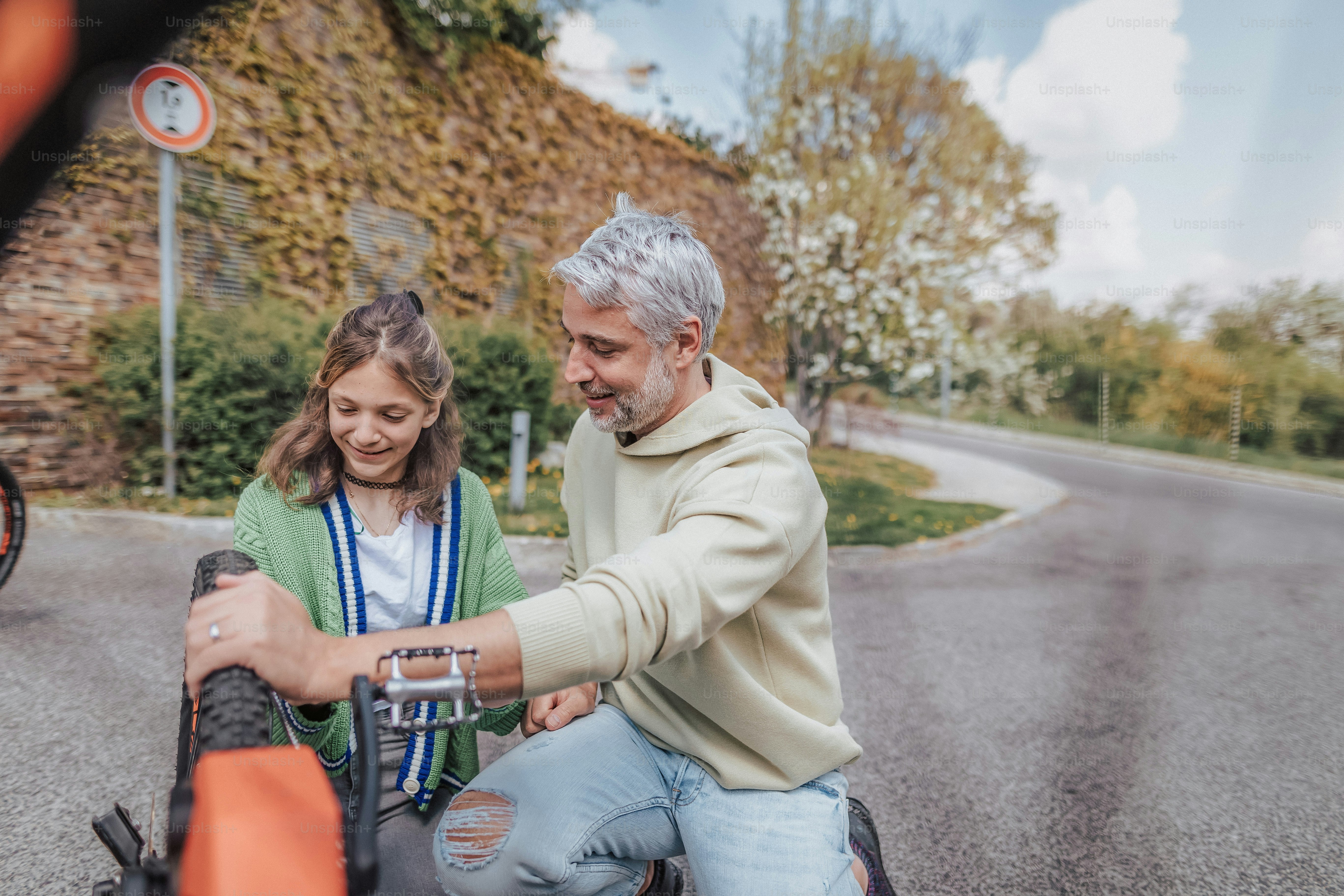 A happy father with teenage daughter repairing bicycle in street in town.A happy father with teenage daughter repairing bicycle in street, high angle view.