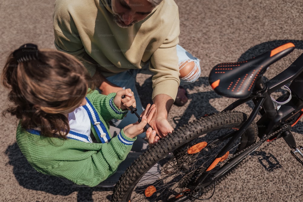 A happy father with teenage daughter repairing bicycle in street, high angle view.