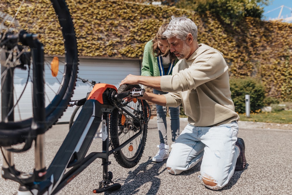 A happy father with teenage daughter repairing bicycle in street.A happy father with teenage daughter repairing bicycle in street, high angle view.