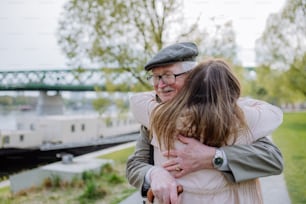 Una vista trasera de una hija adulta abrazando a su padre mayor cuando se encuentra con él al aire libre en la calle.