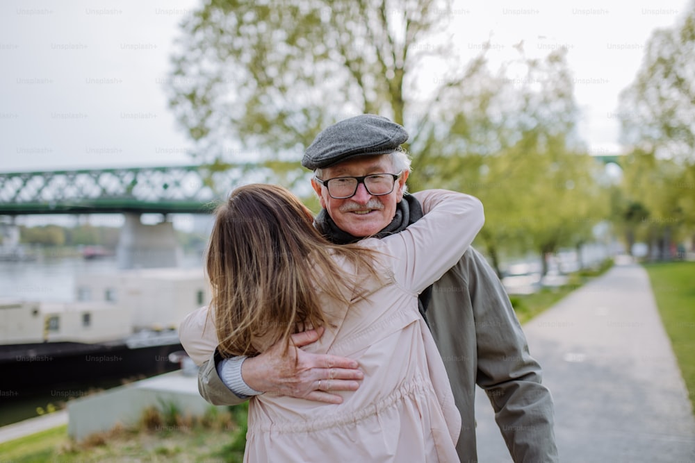 Una vista posteriore della figlia adulta che abbraccia il padre anziano quando lo incontra all'aperto in strada.