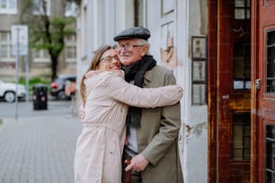 An adult daughter hugging her senior father when meeting him outdoors in street.