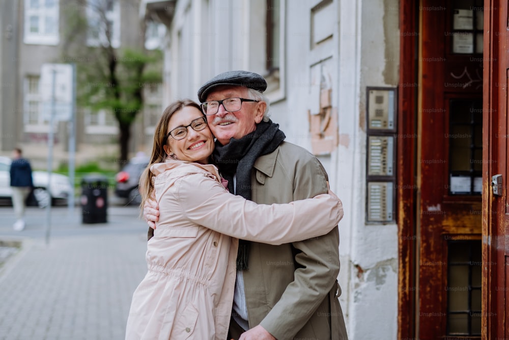 An adult daughter hugging her senior father when meeting him outdoors in street.
