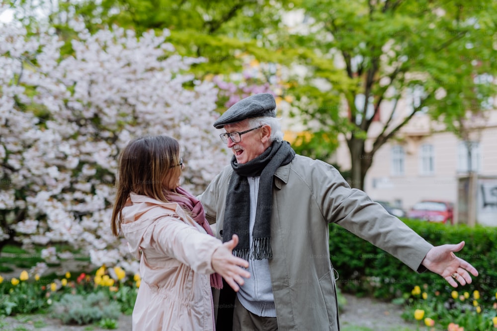 An adult daughter with outstretched hands meeting her senior father outdoors in park on spring day.