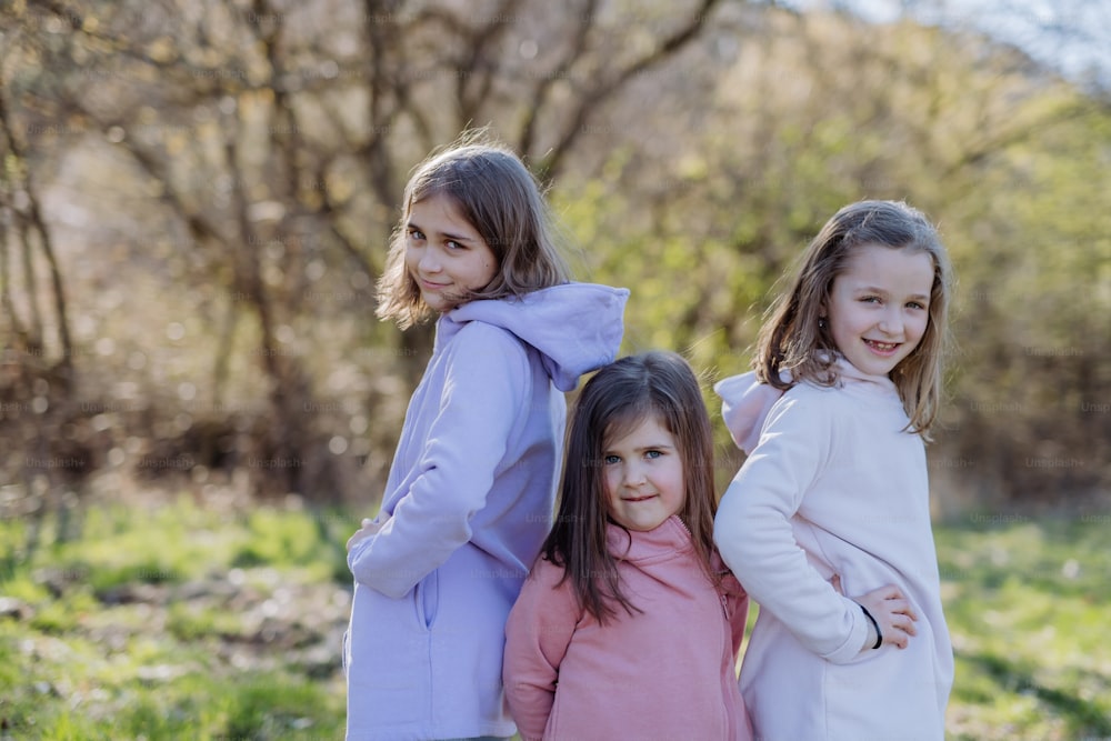 Three little sisters looking at a camera in spring nature together.