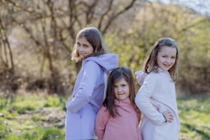 Three little sisters looking at a camera in spring nature together.