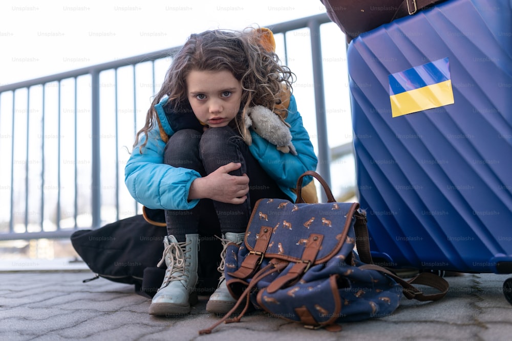 Ein trauriges ukrainisches Einwandererkind mit Gepäck, das am Bahnhof wartet, ukrainisches Kriegskonzept.