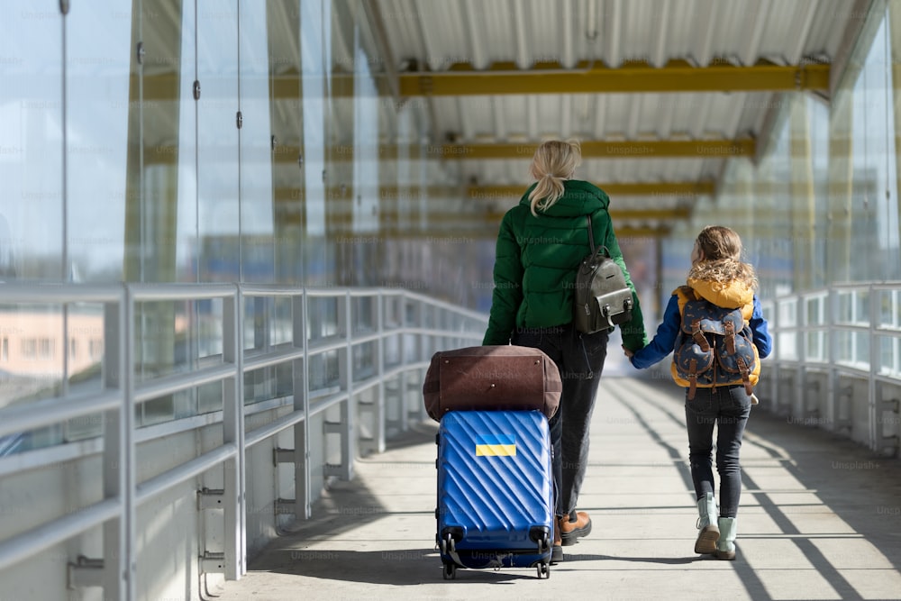 Uma visão traseira da mãe imigrante ucraniana com criança com bagagem andando na estação de trem, conceito de guerra ucraniano.