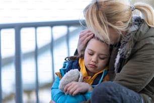 An Ukrainian immigrants mother with daughter with luggage waiting at train station, Ukrainian war concept.