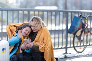 Une mère immigrée ukrainienne avec une fille avec des bagages attendant à la gare, concept de guerre ukrainien.