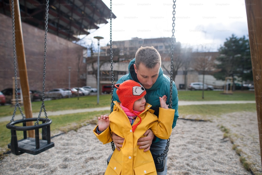 Ein Vater schiebt seine kleine Tochter mit Down-Syndrom auf Schaukel im Freien im Spiel.