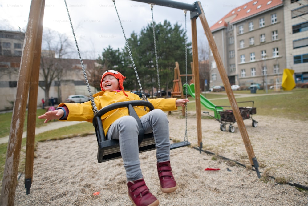 Little girl with Down syndrome on swing outdoors in playgraound.