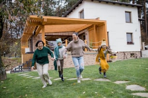 Two happy sisters with a mother and grandmother holding hands and running outdoors in garden in autumn