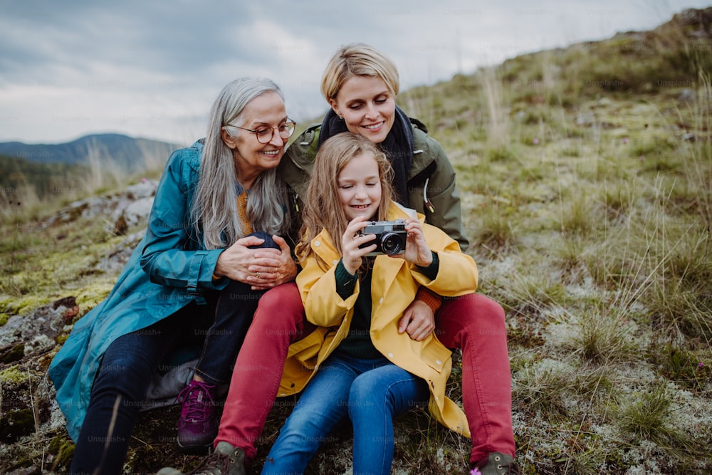 A small girl with mother and grandmother taking selfie pictures on top of mountain.