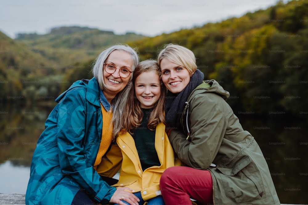 A portrait of small girl with mother and grandmother sitting and looking at camera outoors in nature.