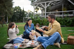 A happy young family sitting on blanket and having take away picnic outdoors in restaurant area.